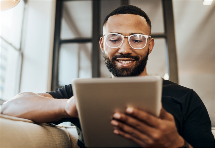 man with glasses smiling while looking at tablet